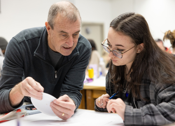 A professor assists a student with a circular diagram.