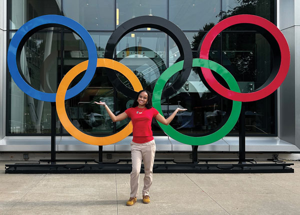 A University of Hartford student stands in front of the Olympics rings smiling.