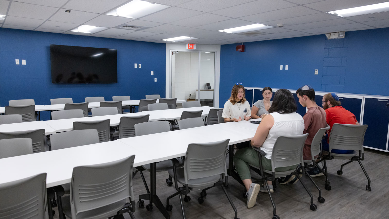 The sitting area that includes long tables and chairs with wheels in the Zachs Hillel Center.